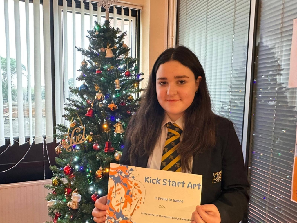 Picture of a Queen Elizabeth's winning student stood in front of a Christmas tree holding a certificate.