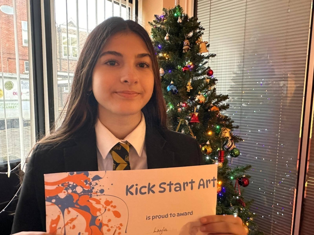 Picture of a Queen Elizabeth's winning student stood in front of a Christmas tree holding a certificate.