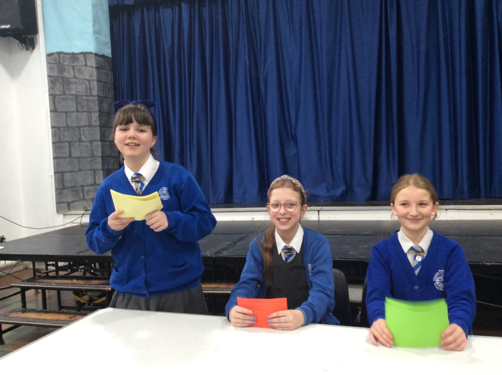 Students from Honiton Community College Hosting Youth Speak Competition 3 students behind a table.