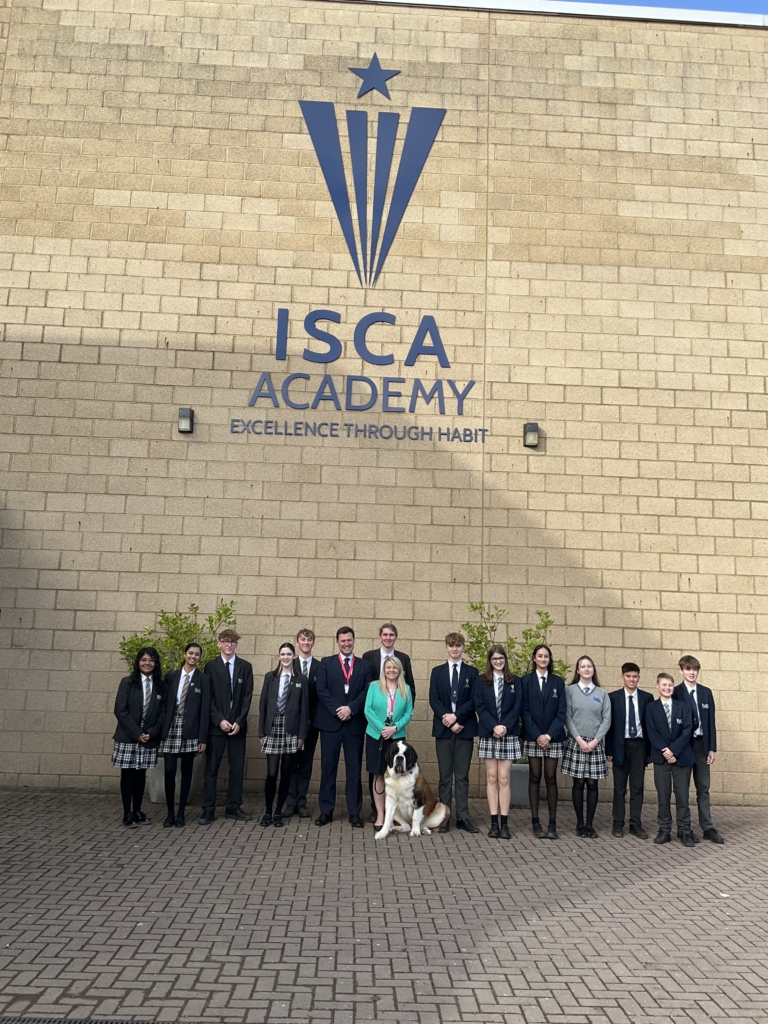 Students from Isca outside the school infront of the Isca School logo with Headteacher and Steve Race MP