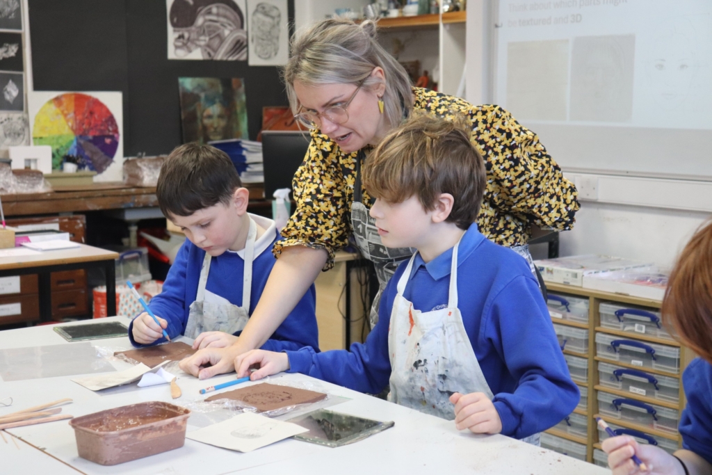 A Primary Pupil making a clay self-portrait at Sidmouth College with teacher helping 