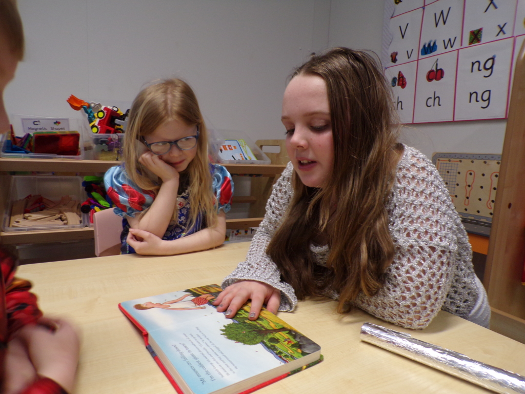 Teacher sitting at table reading to child