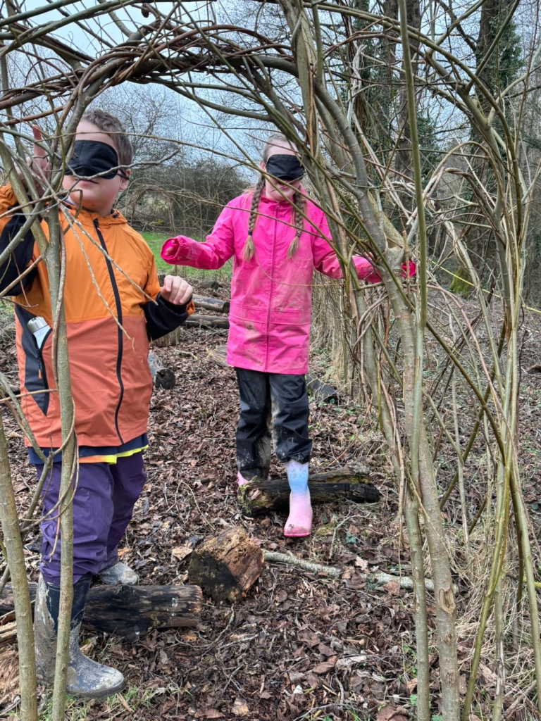 Pupils from Whipton Barton Federation going through a woodland trail with blindfolds on as a teamwork exercise