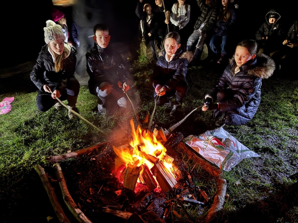 Pupils from Whipton Barton Federation sat around a camp fire at night toasting marshmellows