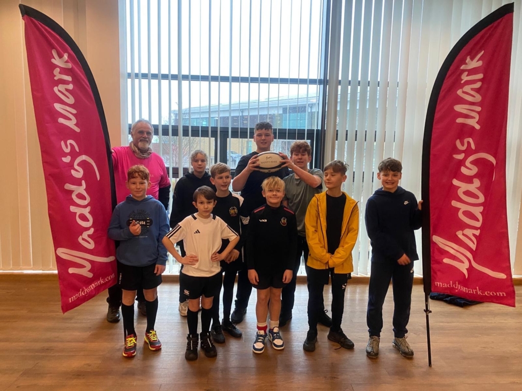 Pupils from Cranbrook Education Campus stood in a conference room at Sandy park, Exeter with two big red flags either side and Exeter Chiefs Coach.