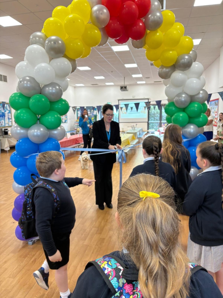 Students watch as CEO cuts ribbon under a balloon arch