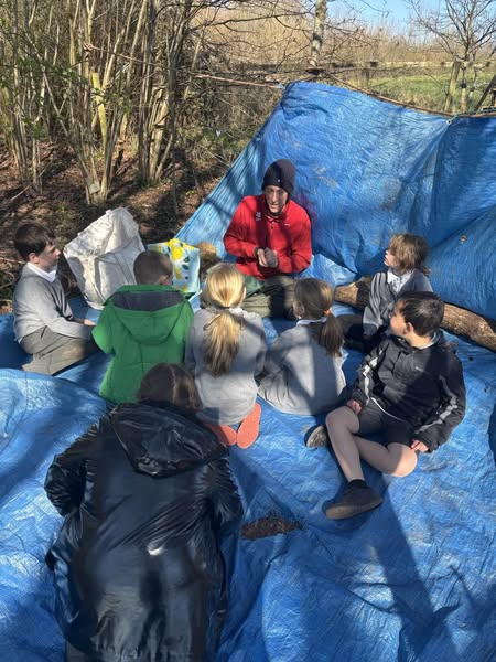 Several children sat on a blue tarpaulin in the forest, listening to a talk
