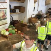 Children in yellow high vis jackets in front of a brown long table, with baskets and fruit and vegetables