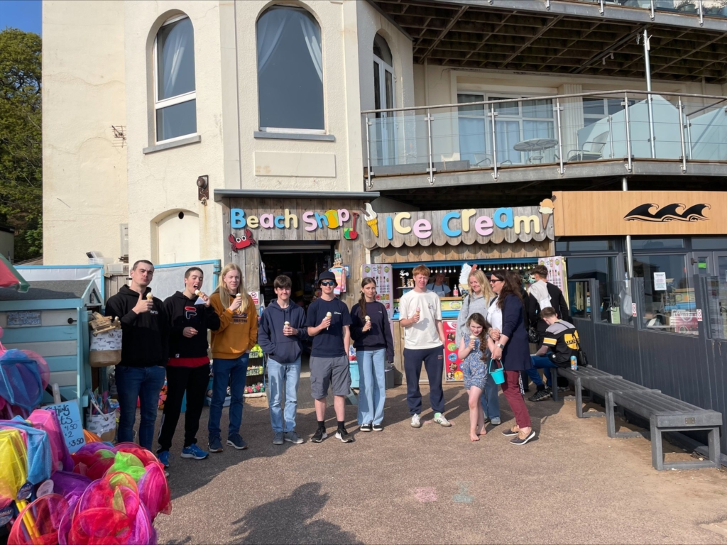 Students stood in a line enjoying ice creams in front of beach ice cream hut