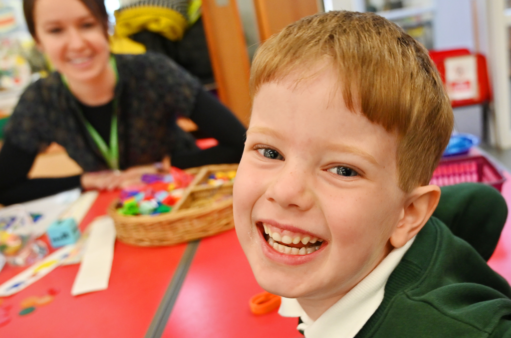 Child smiling into camera, sat at red table