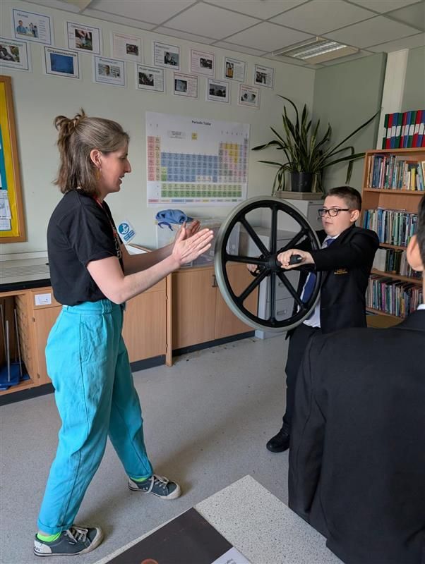 Woman stood on left holding out hands towards student stood on the right holding a wheel