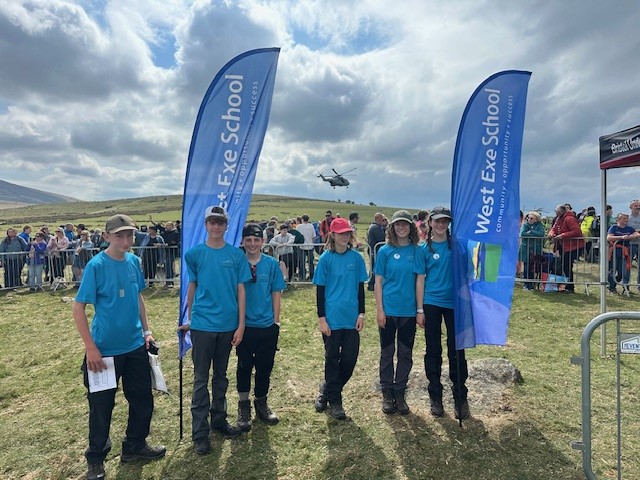 West Exe Team stood with flags either side of them and helicopter in the background at the start of the Ten Tors