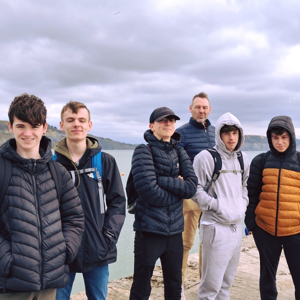 Tor Bridge High Students stood on the beach at Lyme Regis with a teacher. 