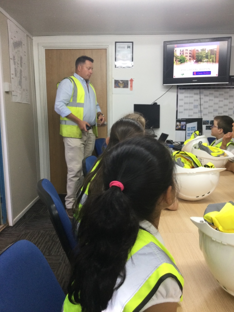 Children sat around a table in high vis jackets in front of a tv screen