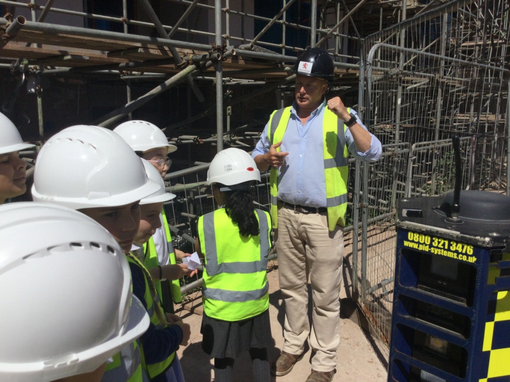 Children stood with hard hats and high vis jackets listening to a speech from a building manager