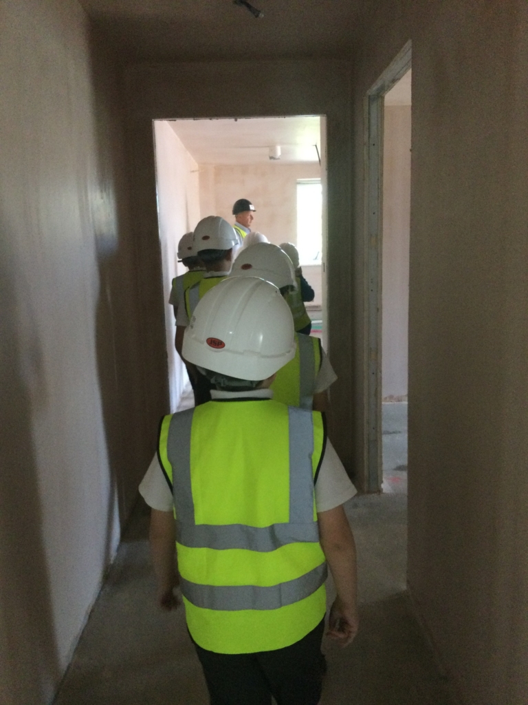 Row of children in hard hats walking down a corridor