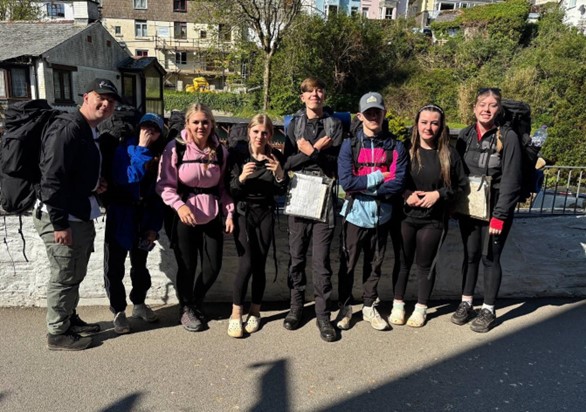 A group of students stood in the street posing for a photograph with their hiking backpacks on