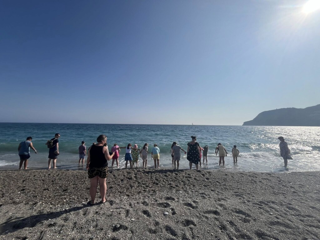 Students wading in the shallows of the sea, with sand in the foreground of the photo