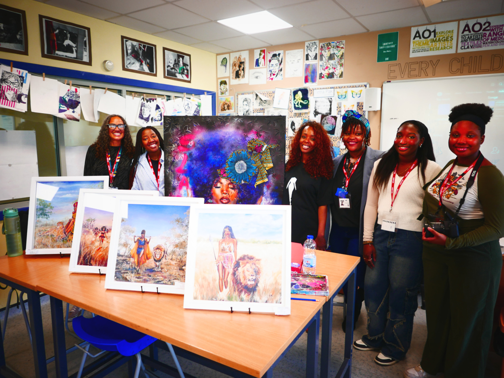 Art displayed on a table in front of students standing and smiling with workshop leader