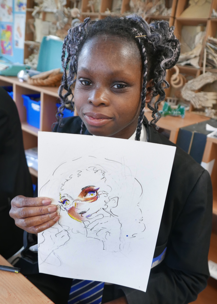 One student looking at camera holding up their drawing in front of them of a girl on a white piece of paper