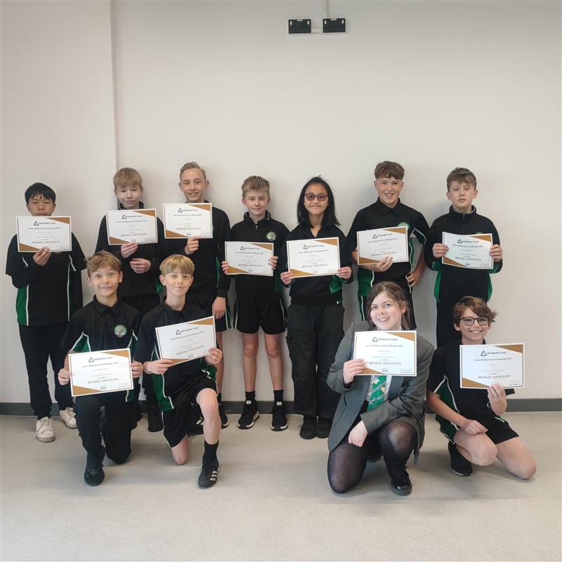 Students in school uniform holding up certificates in front of white wall