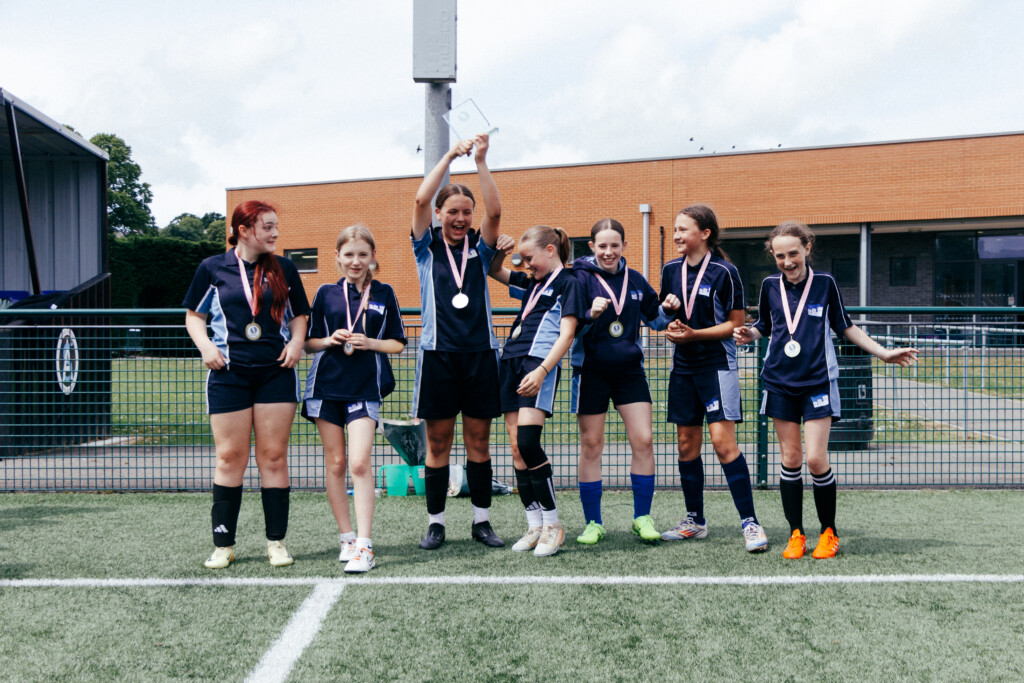 Six girls in blue football kits celebrating win with medals round their neck