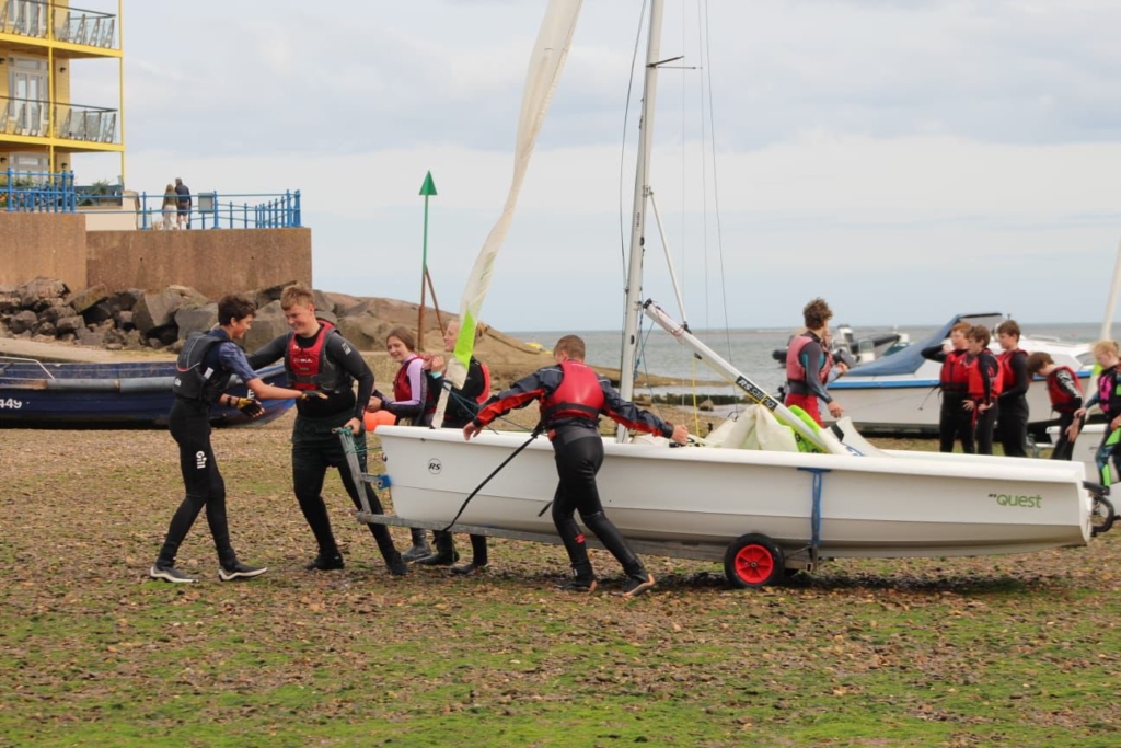 A selection of students in wetsuits and life jackets pulling in their white boat