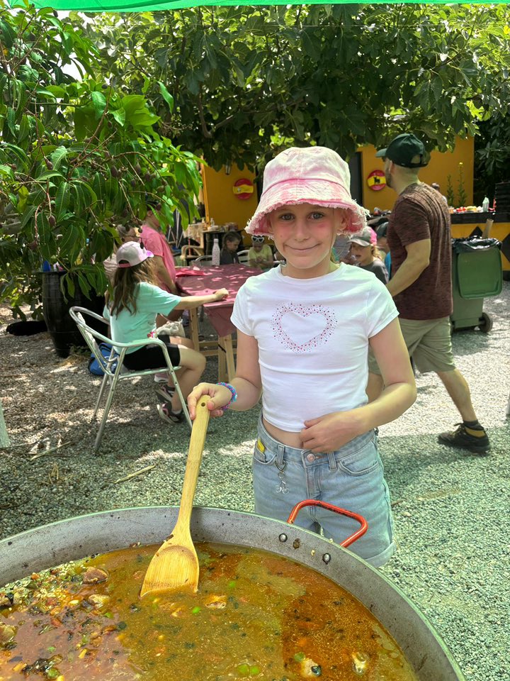 One student stirring a big pan of paella in a garden
