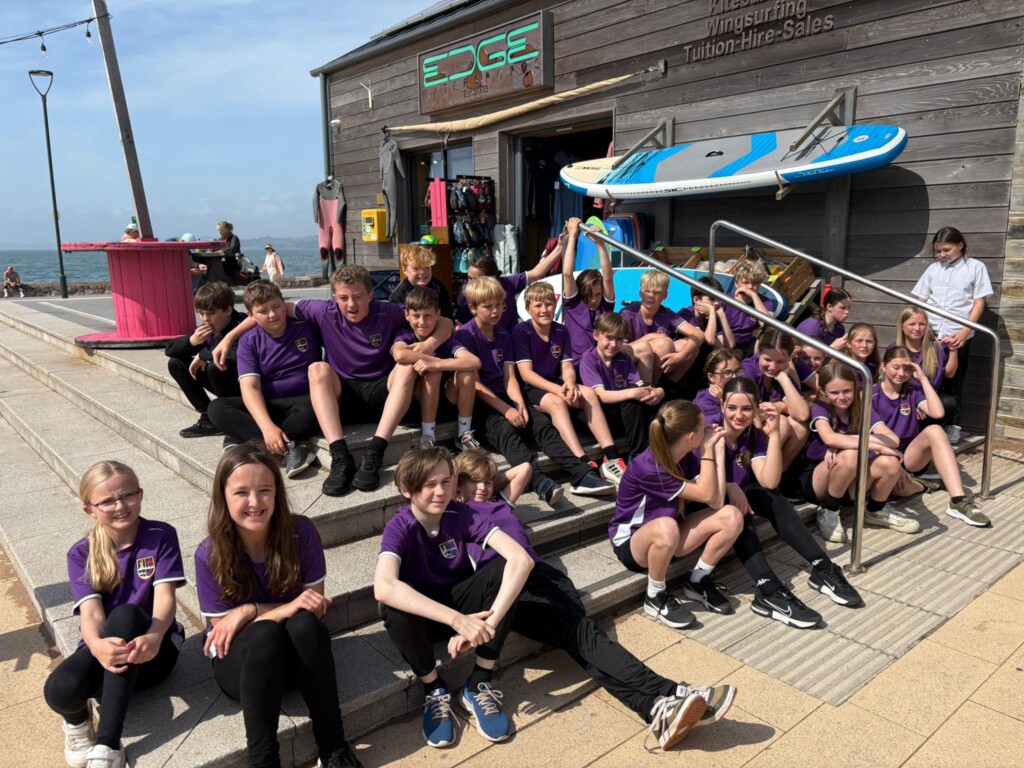Students sat on steps outside a wooden hut at the beach smiling at the camera