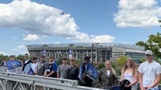 Students stood in a line facing the camera smiling with the rugby stadium in the background