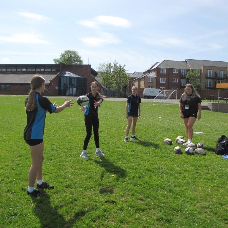 Female students on grass stood in a line passing rugby ball