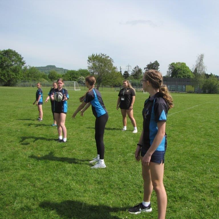 Female students on grass stood in a line passing rugby ball