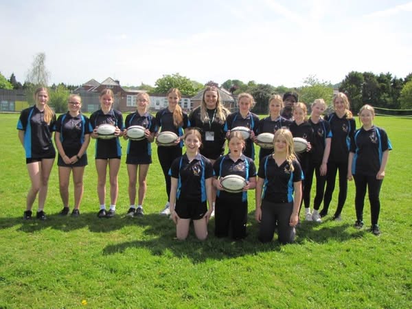 Female students stood in line on grass facing camera holding a rugby ball