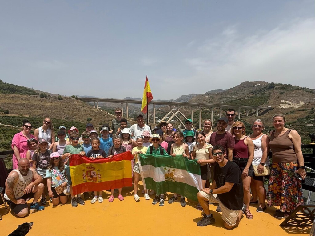 Students stood in a group holding spanish flag. In the distance is hills and a long bridge