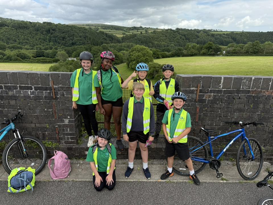 Students in high vis jackets and cycle helmets posing in front. Green fields and trees are in the distance