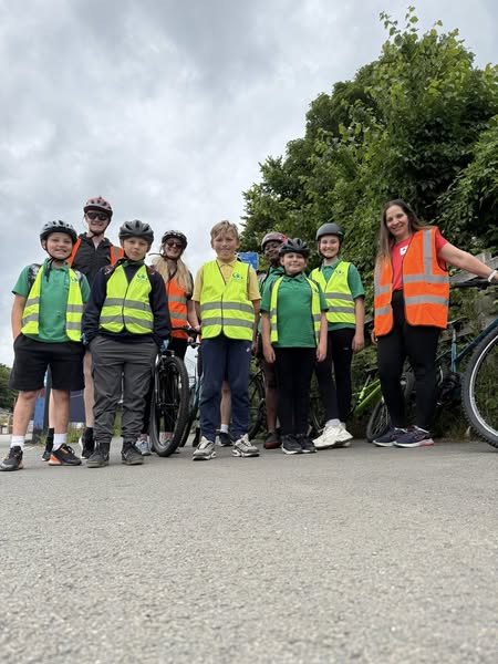 Students in high vis jackets stood on pavement with bike helmets on facing camera