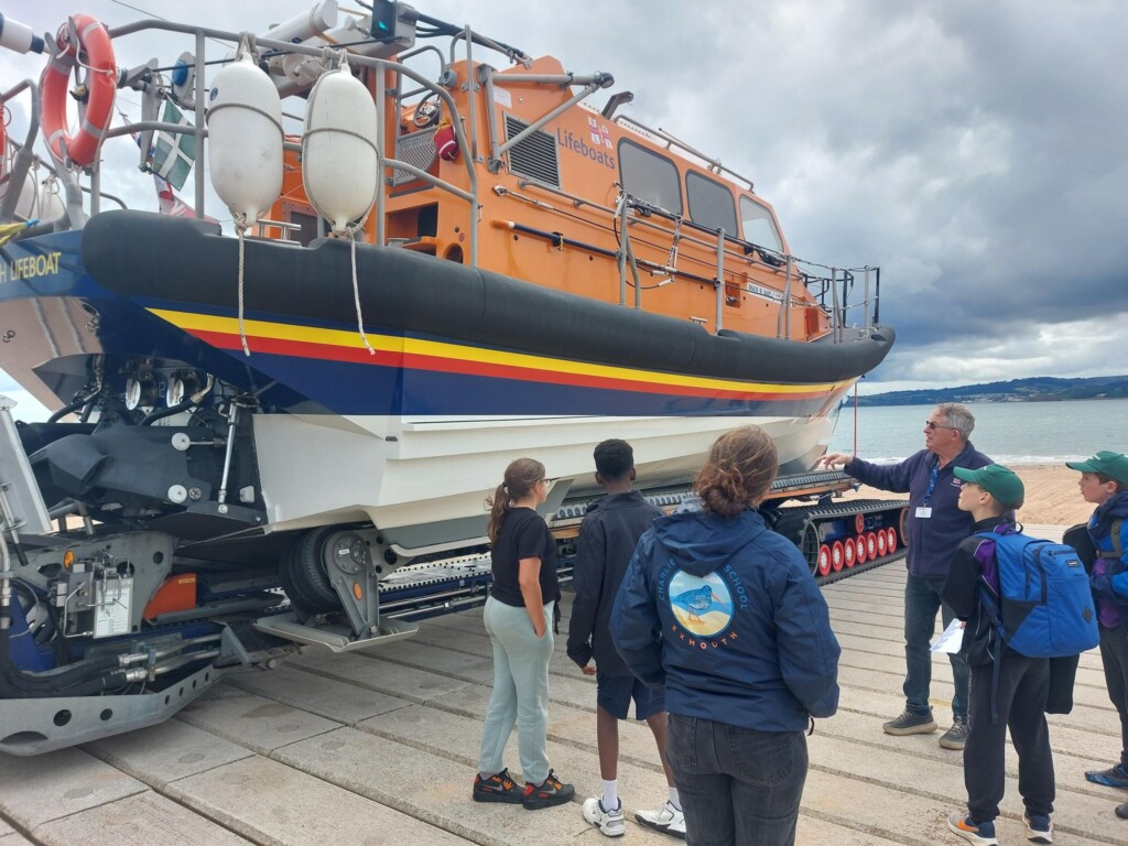 The back of three students looking at the RNLI lifeboat.