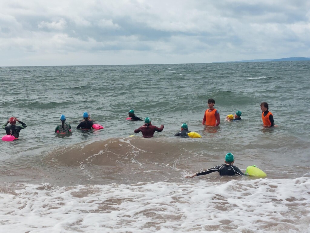 Students in the sea in wetsuits and swimming caps swimming