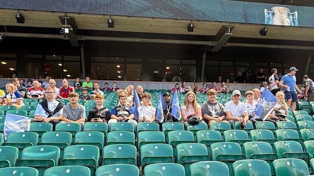 Students sat at the rugby ground in a line on green chairs.