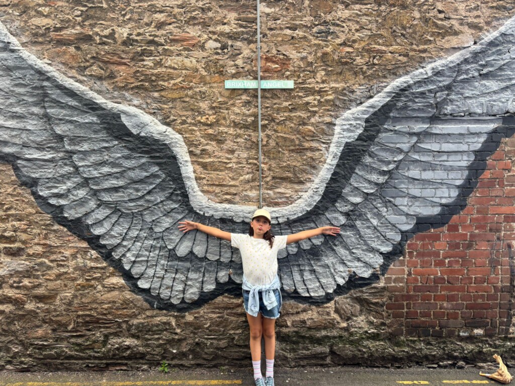 Child stood with arms outstretched against a wall with angel wings painted