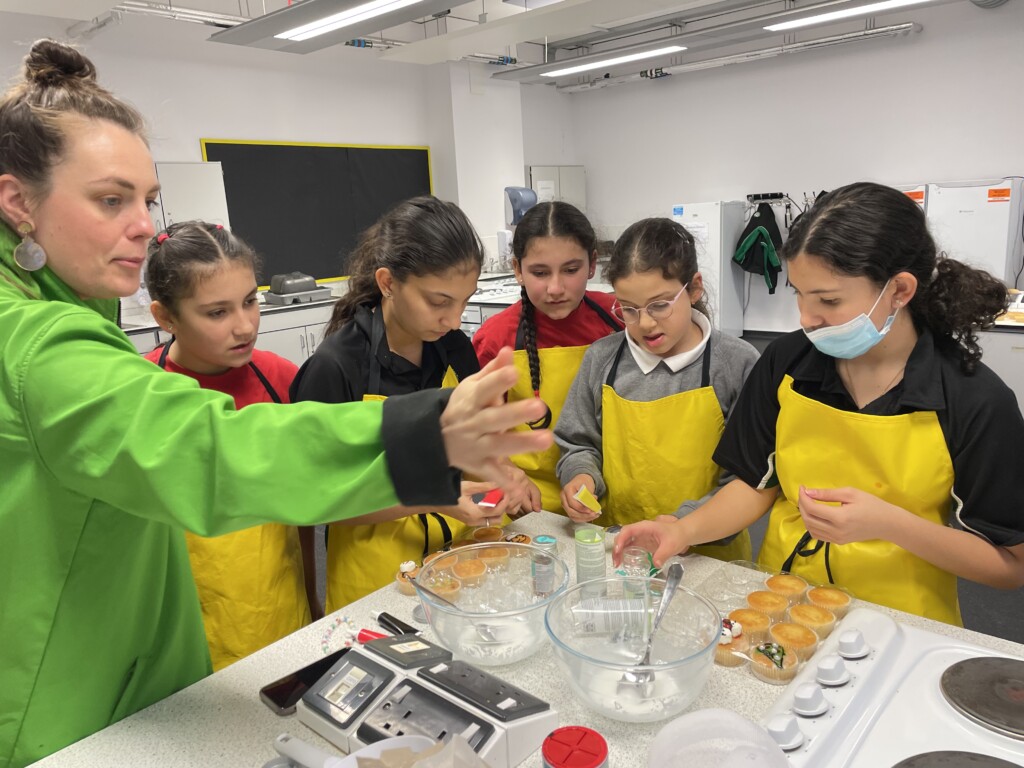 Students stood in group around kitchen counter baking.