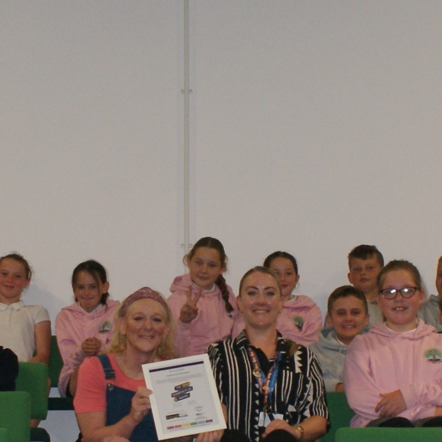 Two teachers holding an award certificate surrounded by students
