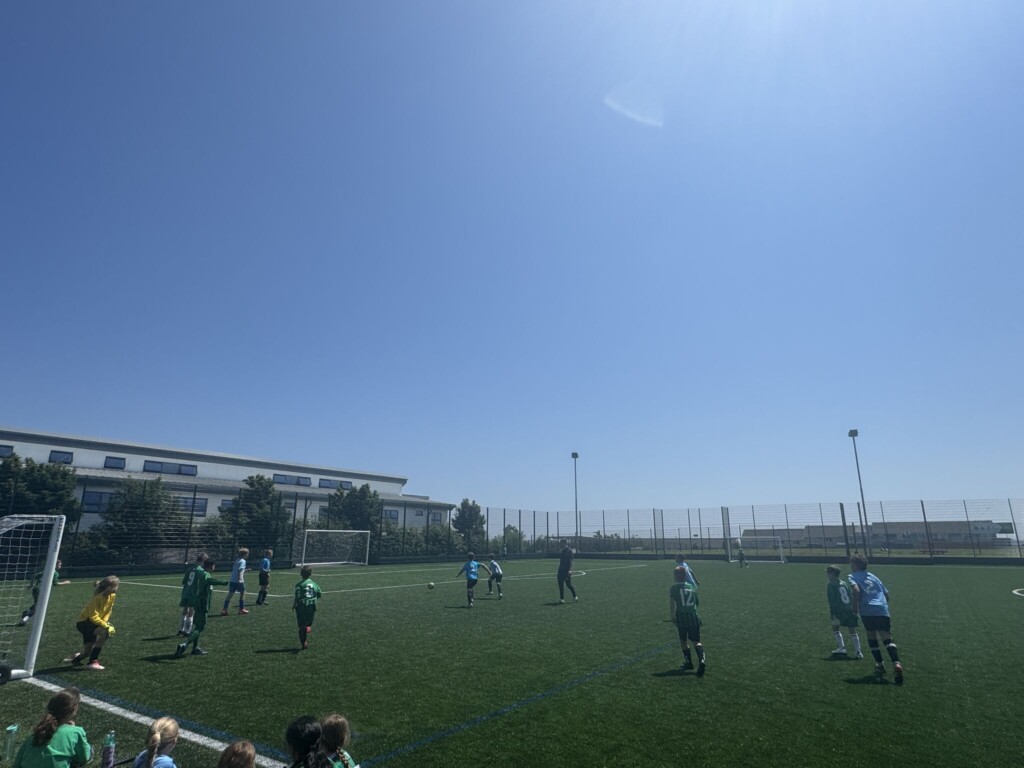 Photo of a football pitch with children playing under a blue sky.