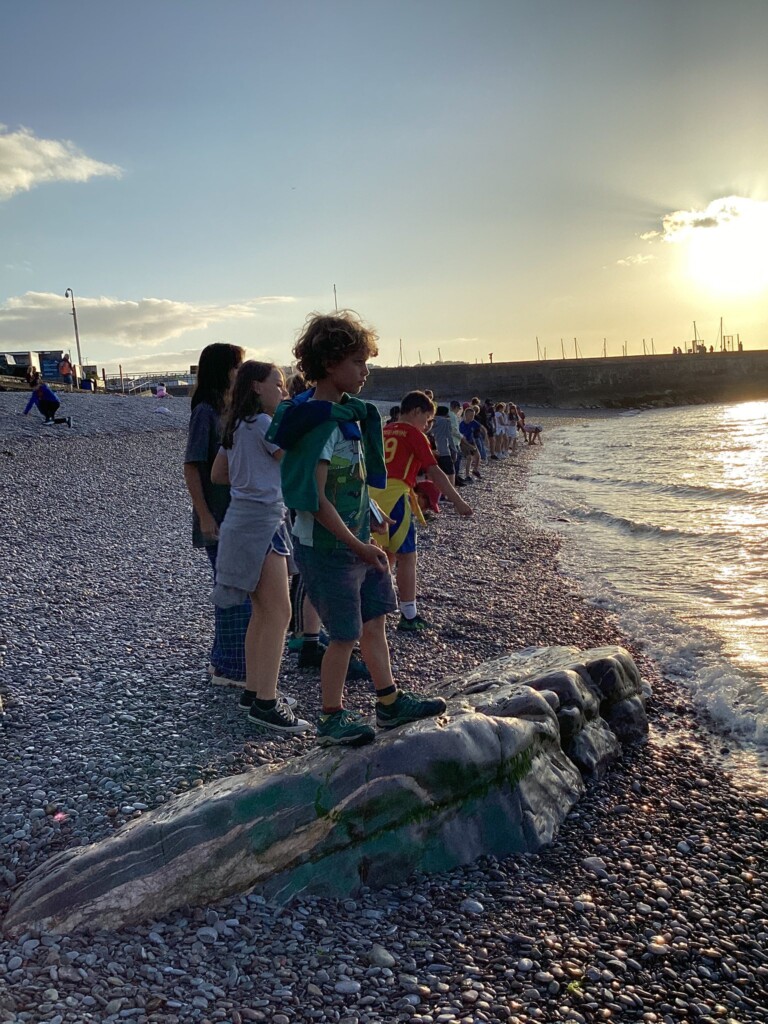 Row of children stood on the beach at the edge of the water in the sunset
