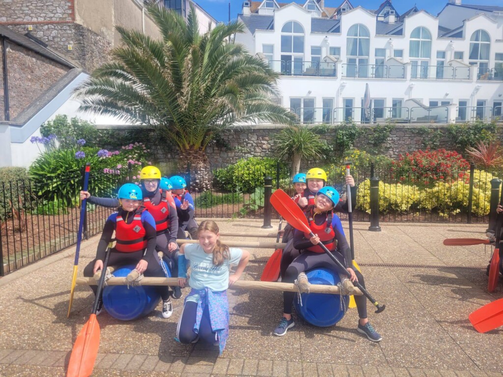 Children in life jackets and helmets sat on makeshift raft and holding oars