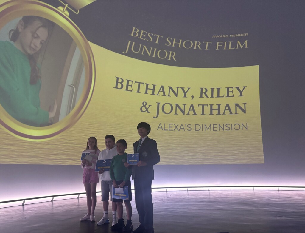 Four students stood in front of screen holding certificates