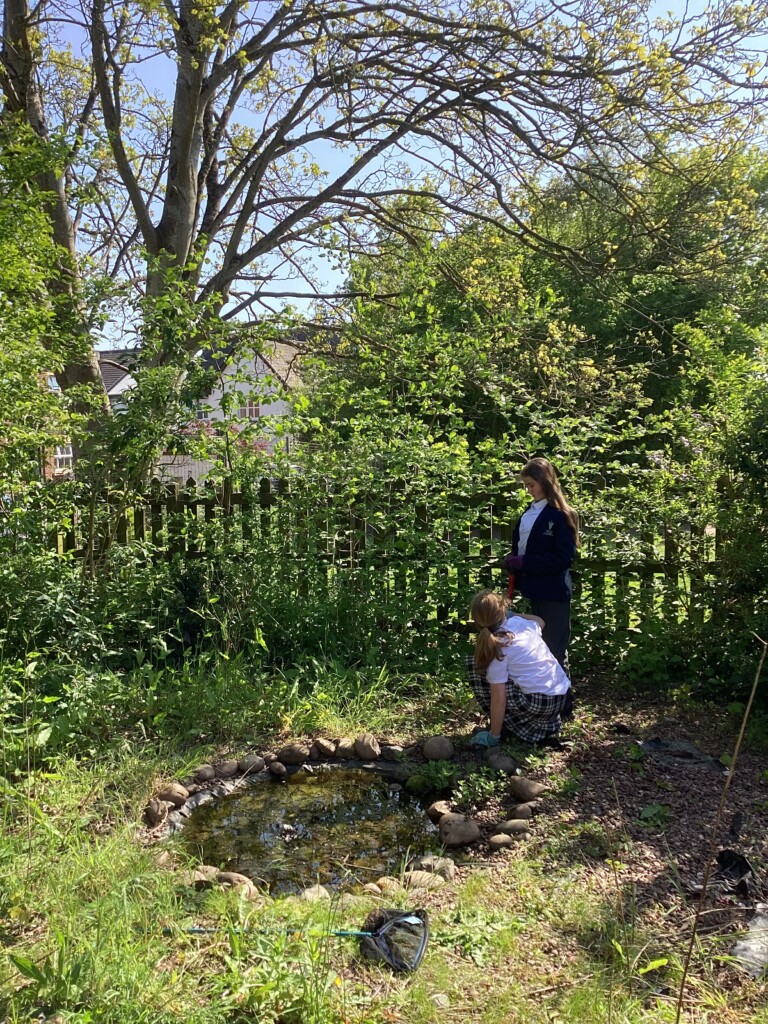 Two students in their uniform gardening in the grass
