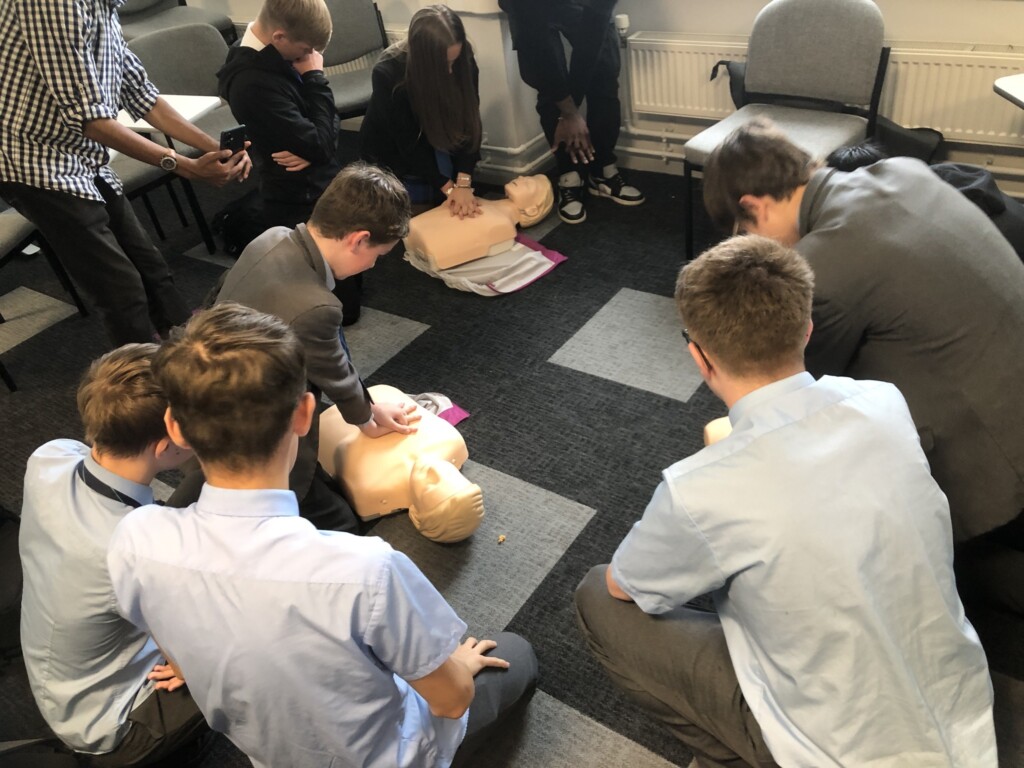 Students kneeling on a gray floor practicing CPR on a dummy