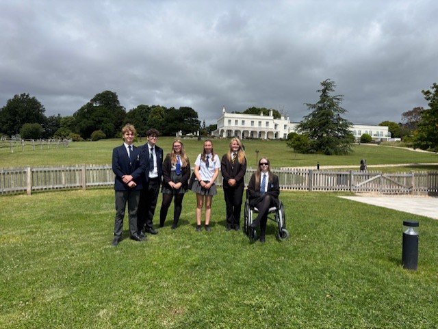 Six students on grass in front of white manor house