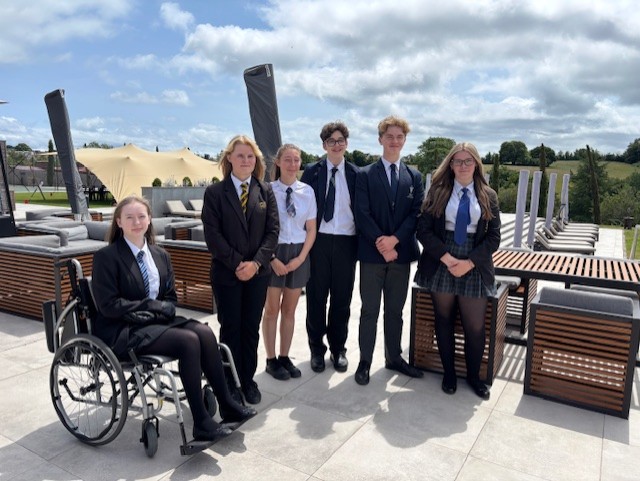 Six students on a patio in front of garden furniture